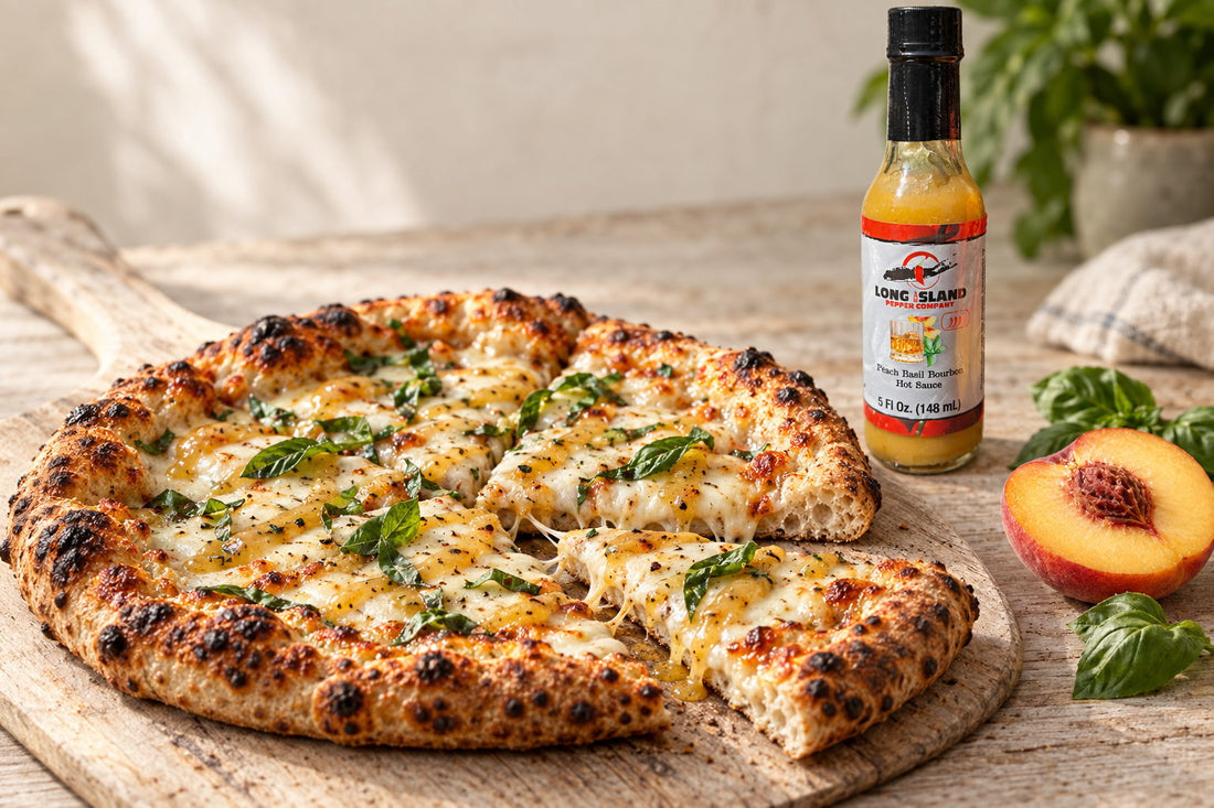 A wood-fired white pizza with basil and a pale gold sauce, with a bottle of Peach Basil Bourbon hot sauce behind